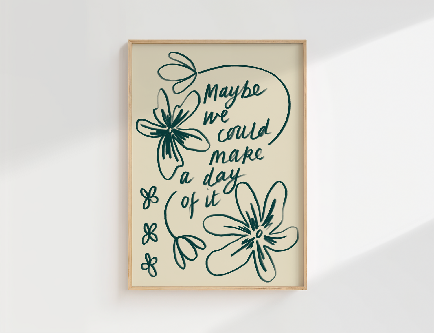 Framed artwork with the handwritten quote ‘maybe we could make a day of it’  with loose hand drawn flowers, set against a white wall.