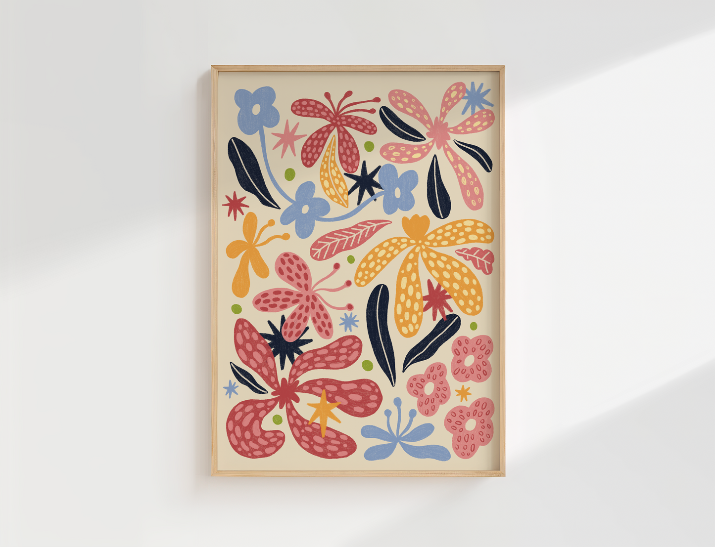 A framed art print featuring a colourful retro floral pattern with abstract flowers and leaves on a cream background, housed in a light natural wood frame and displayed on a white wall.