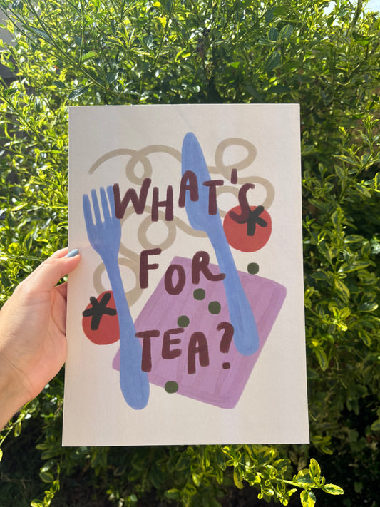A hand holds an A4 art print featuring a whimsical illustration of a pink napkin, blue cutlery, red tomatoes, and green peas with the text 'WHAT'S FOR TEA?' on a cream background, in front of green garden foliage.