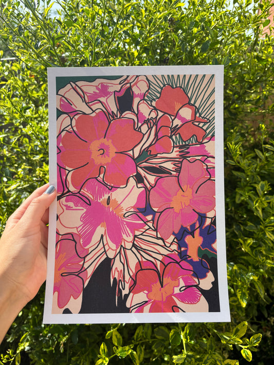 A hand holds an A4 art print featuring a vibrant floral design with pink, coral, and magenta flowers outlined in black, set against a background of green garden foliage.